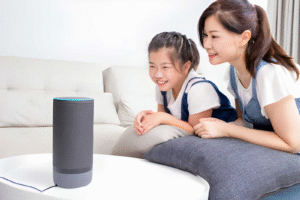 A mother and daughter happily looking at a cylindrical smart speaker in their living room.