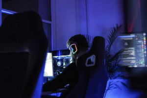 Person wearing RGB gaming headphones sitting at a computer in a dark blue room.