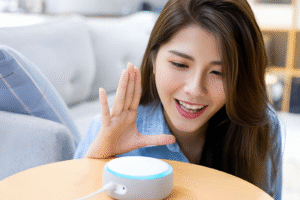 A woman smiling and interacting with a small, circular smart speaker on a table.