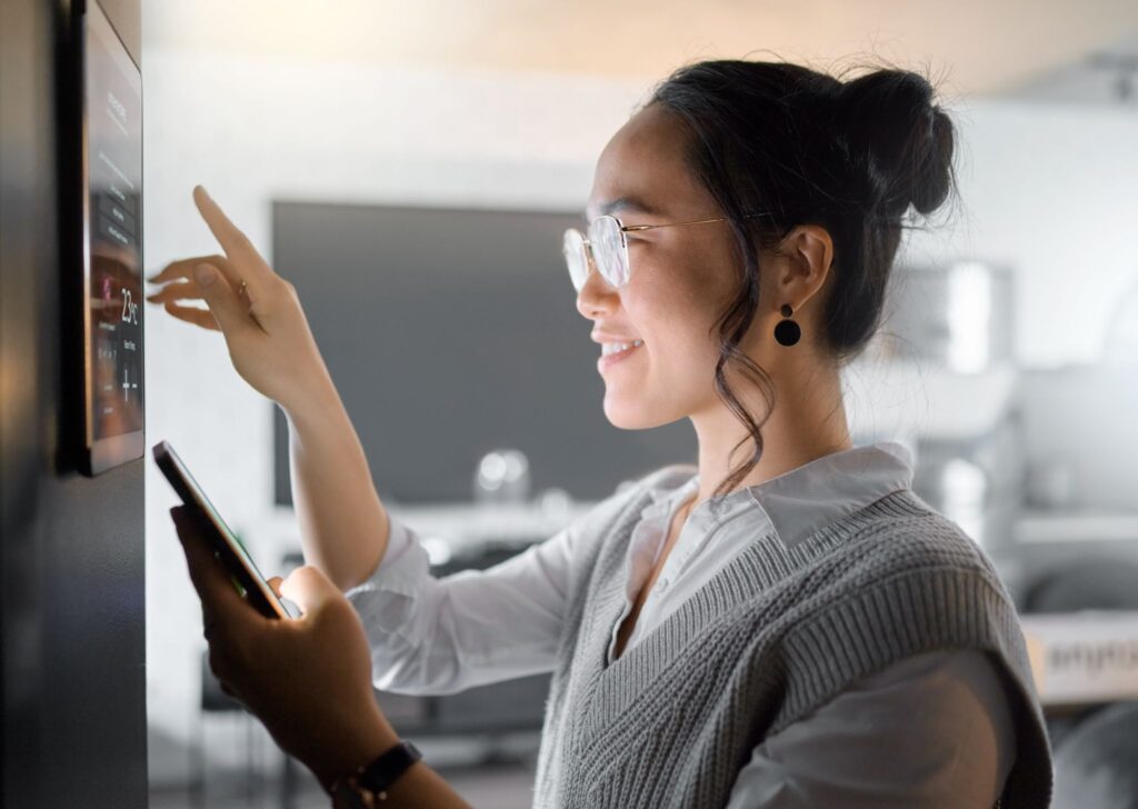 why-your-smart-home-needs-regular-maintenance a woman using a smart home automation application on a tablet that is plastered on the wall